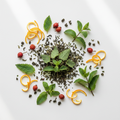 A styled overhead flat-lay of loose green tea leaves arranged in a circular pattern on a white surface, surrounded by fresh mint leaves, orange zest curls, and small red berries.